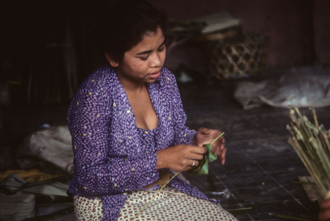 Woman wearing purple jacket and batik skirt makes ritual offering