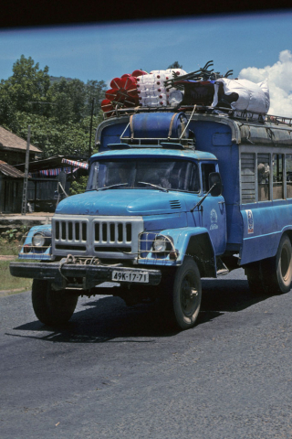 Front of blue bus with rooftop cargo on road from Dalat to Ho Chi Minh City