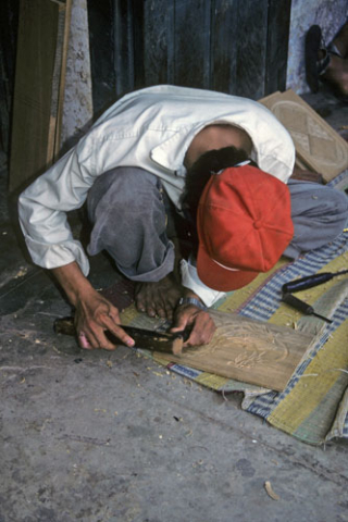 Man carving wood plaque for sale at handicraft workshop in Hoi An